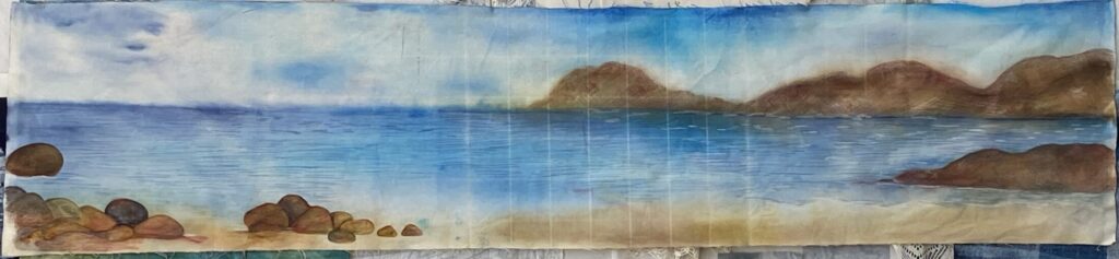 image showing a long and skinny piece of work painted on duck canvas.  The scene shows the ocean with mountains in the background to the right, and then piles of rocks on the left.  work in progress