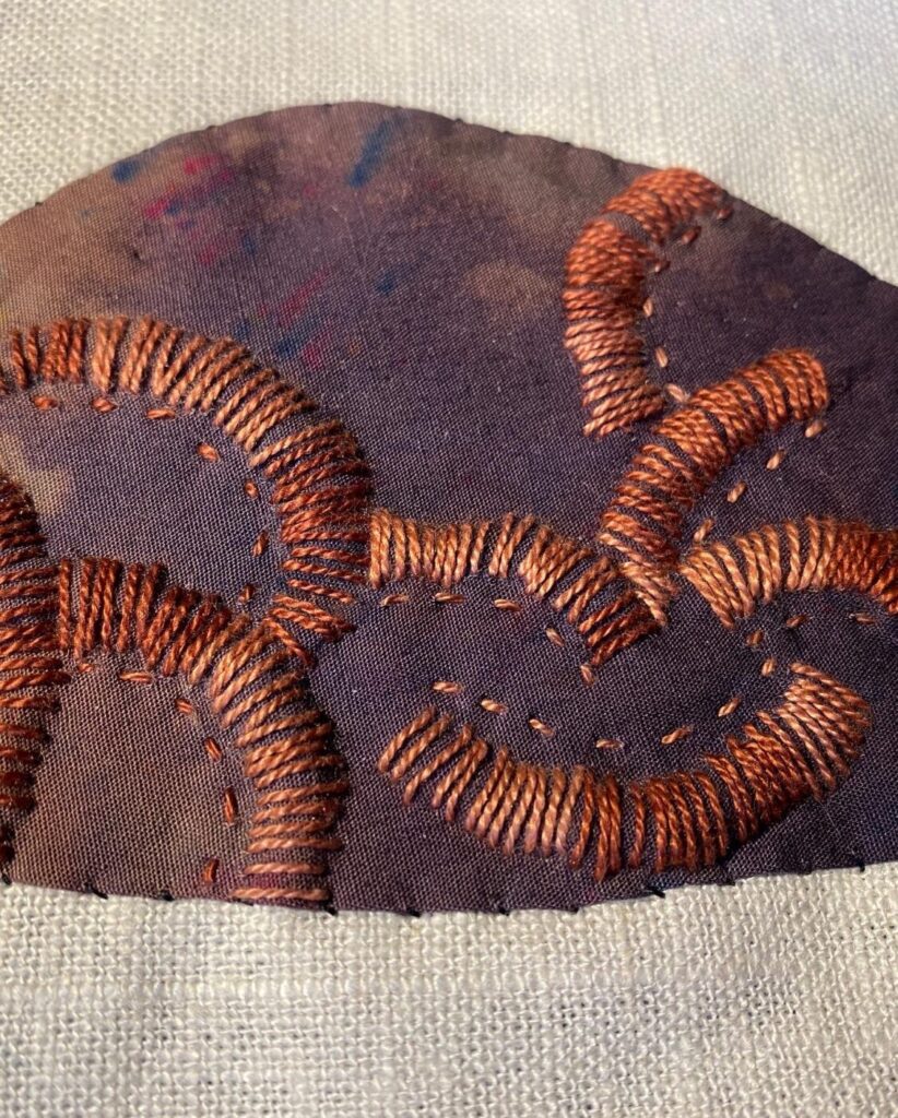 embellished rock with dark brown background and golden brown stitching in circular pattern