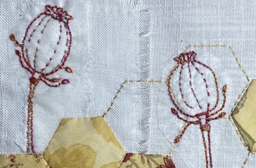 detail - a collage of fabrics on linen with yellow hexies appliqued as a flower and then 2 poppy seed pods are hand-stitched on top with one leaf