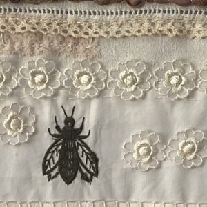 an image showing a detail of a slow stitched scroll with vintage and antique lace and a cicada embroidered in dark thread