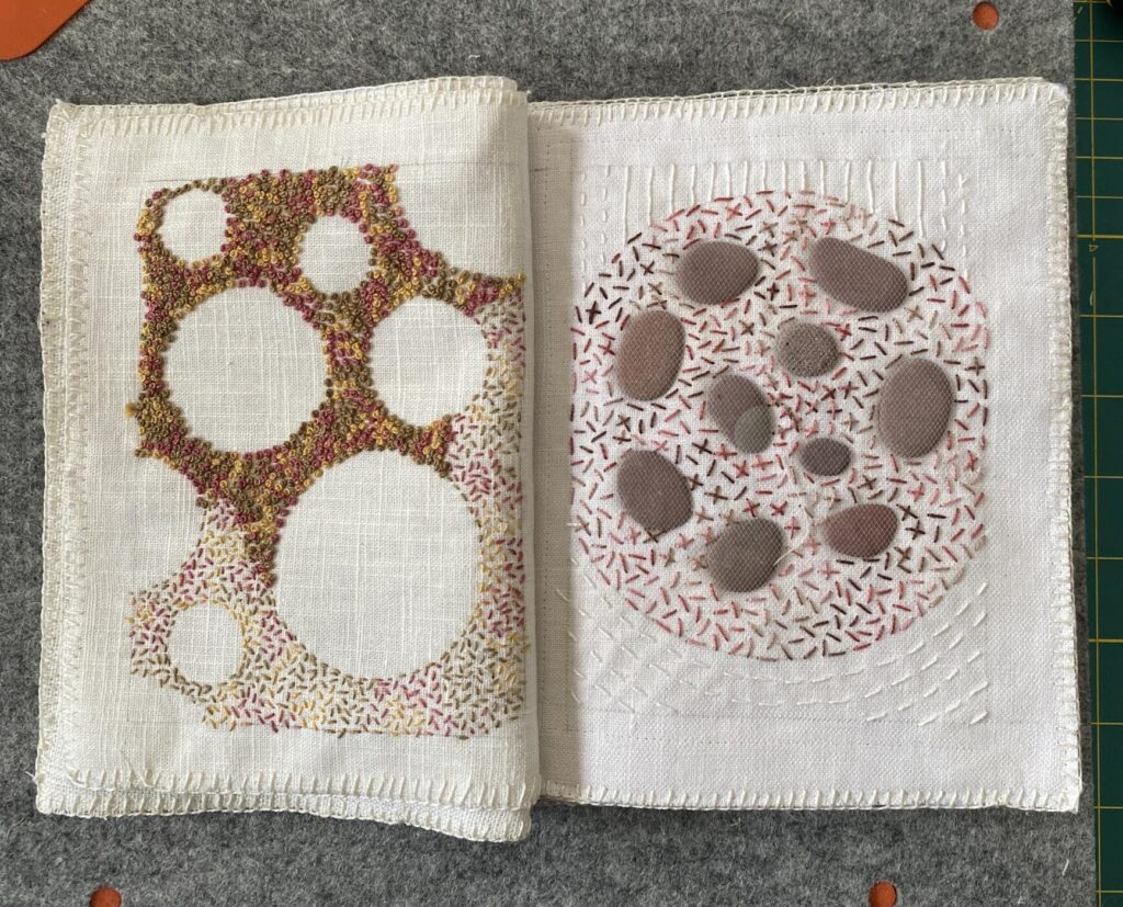 an image showing one of the page spreads. on the right, a circle with real flat small rocks appliqued among crosses and seed stitches and on the left, circles surrounded by colonial knots and seed stitches