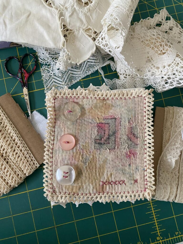 An image showing the cover of a concertina book using a soft piece of old quilted indian fabric. the piece also has three buttons and is surrounded by thin lace.