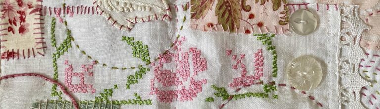 an image showing a detail from the first 2-page layout on the concertina book showing the small napkin with the cross stitched design in pink for the rose and green for the leaves. Plus some added fabrics and a few vintage buttons