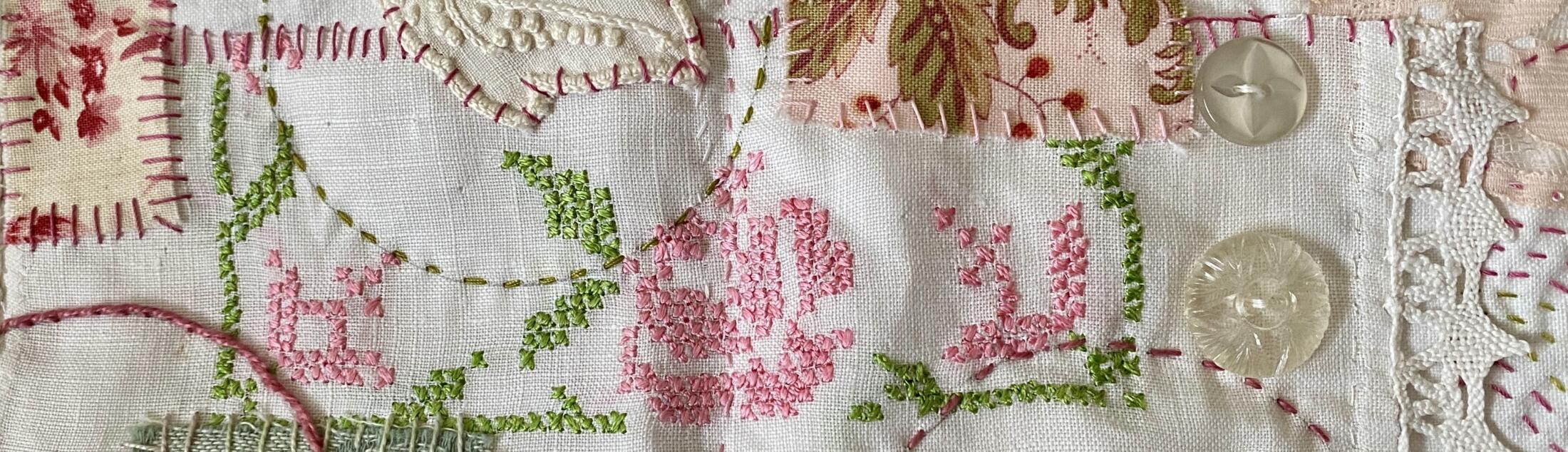 an image showing a detail from the first 2-page layout on the concertina book showing the small napkin with the cross stitched design in pink for the rose and green for the leaves. Plus some added fabrics and a few vintage buttons