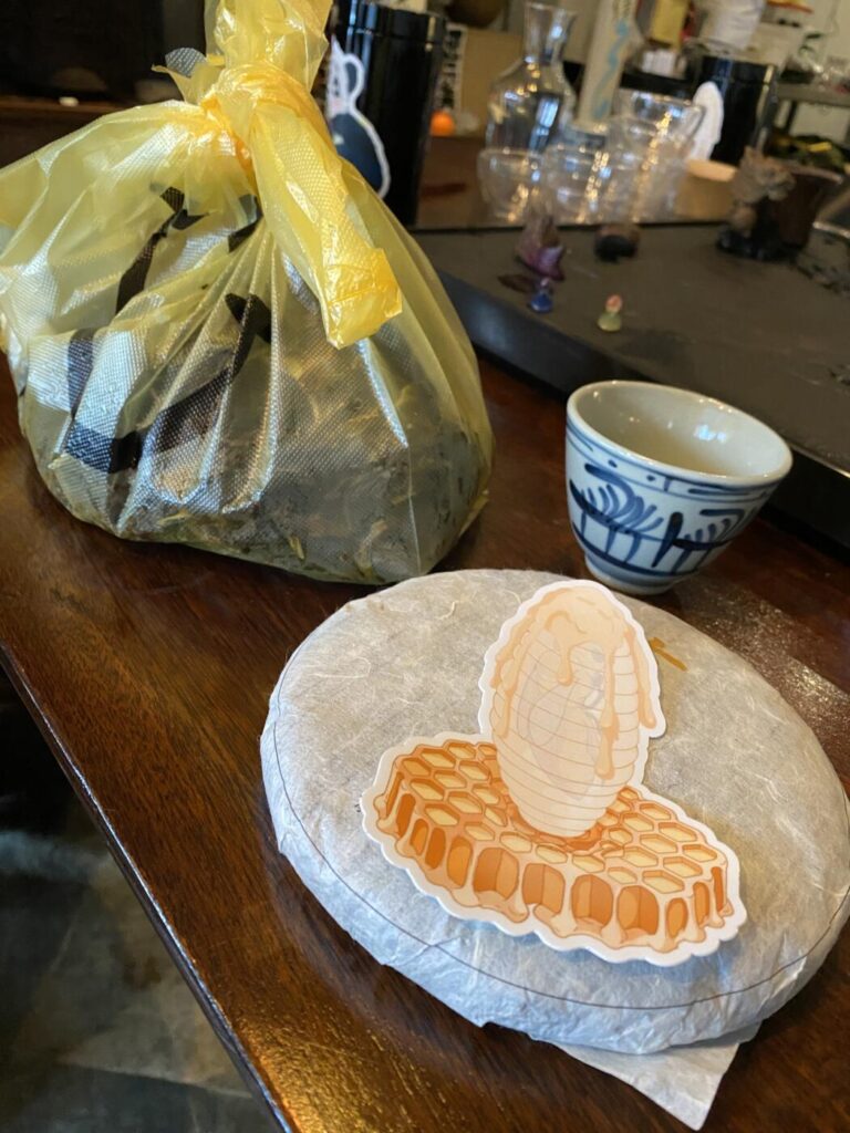 a photo showing a cake of tea, a beautiful cup and a bag of tea leaves