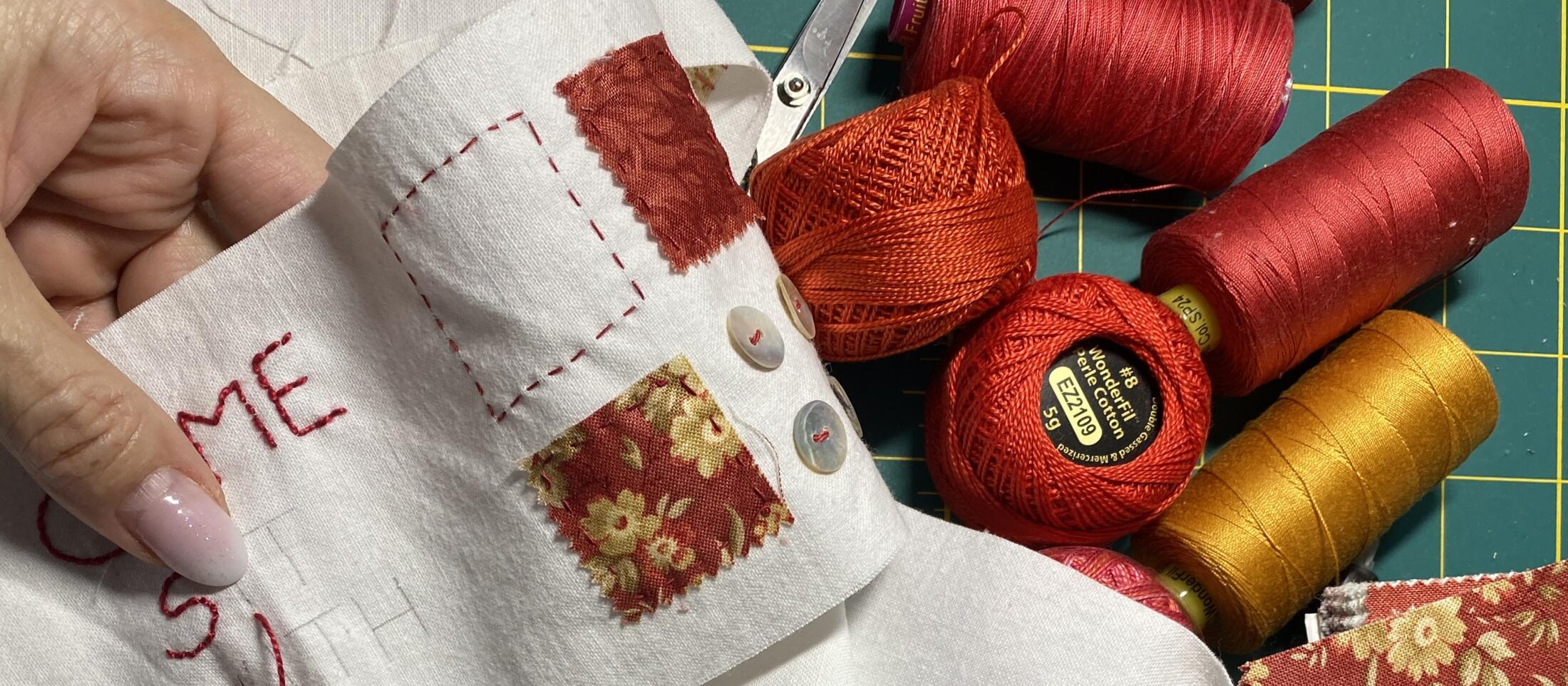 a detail of a hand stitching on a scroll. spools and balls of thread sitting nearby