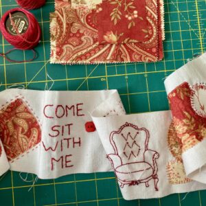 an image showing part of the scroll of fabric with the stitching and pieces of fabric attached to it. A vintage chair has been stitched and it reads come sit with me. a red button completes the composition
