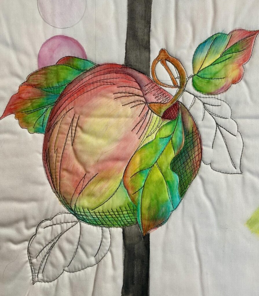 an image showing an apple and leaves free-motion quilted onto a white background and then partially painted with Inktense Pencils