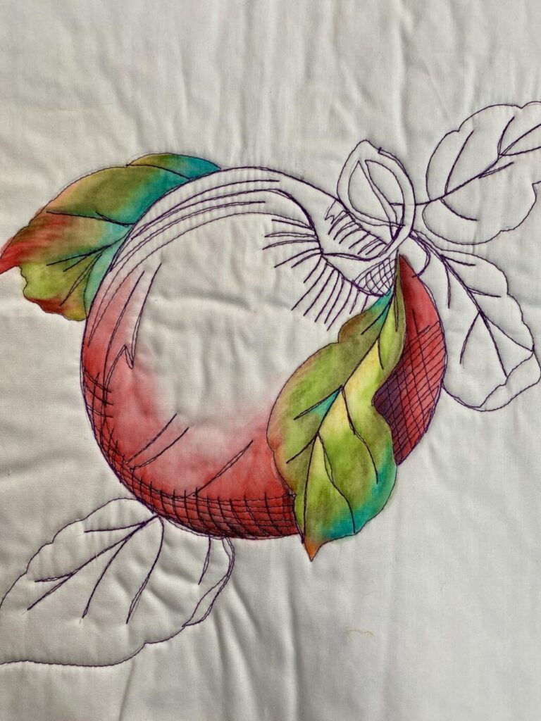 an image showing an apple and leaves free-motion quilted onto a white background and then partially painted with Inktense Pencils