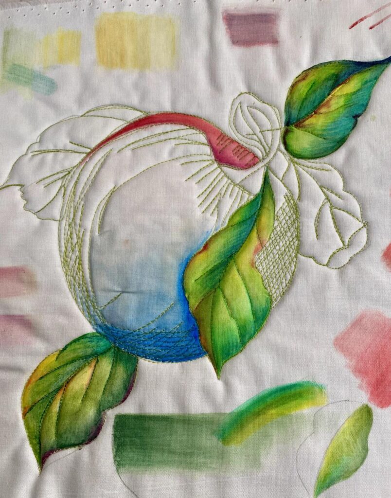 an image showing an apple and leaves free-motion quilted onto a white background and then partially painted with Inktense Pencils